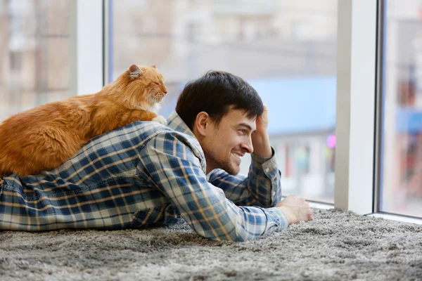 Young man with fluffy cat lying on a carpet