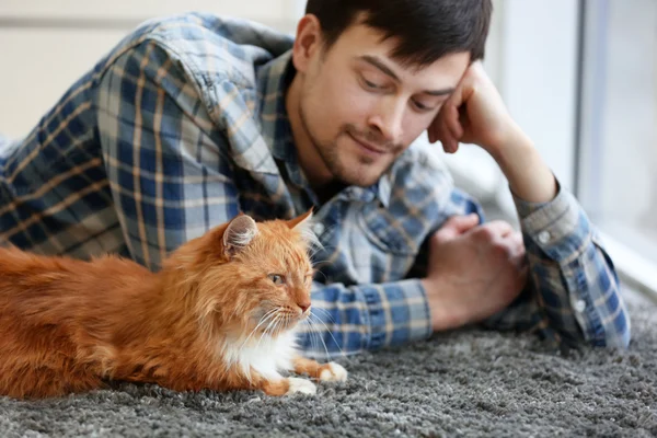 Молодой человек с пушистым котом лежит на ковре — стоковое фото