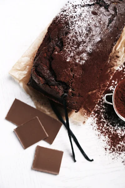 Chocolate cake with cocoa powder, vanilla pods on white table — Stock Photo, Image