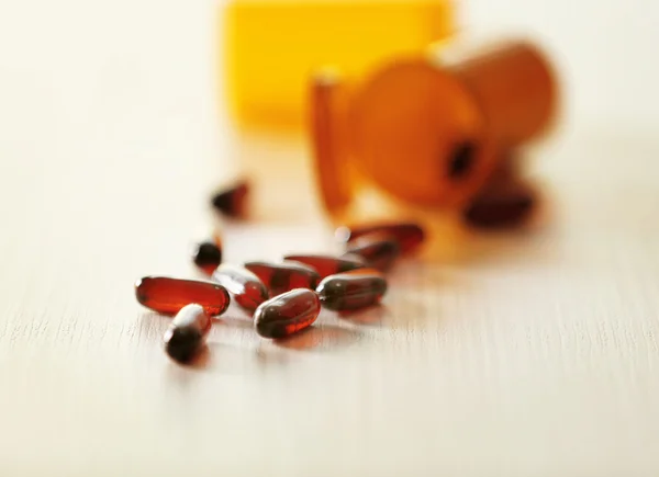 Различные капсулы, пролитые из бутылок с оранжевыми таблетками на деревянный стол, крупным планом — стоковое фото