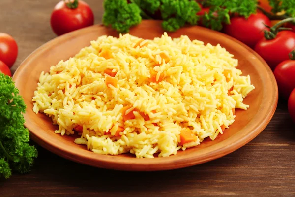 Geschmorter Reis mit einer Karotte auf einem braunen Teller über Holzgrund, Nahaufnahme — Stockfoto