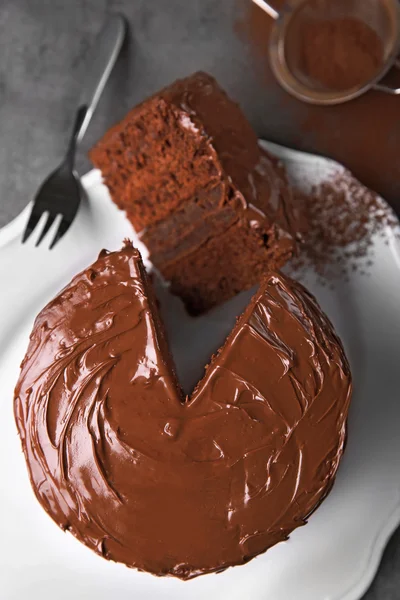 Chocolate cake on plate with a cut piece and fork and cocoa on gray background, closeup — Stock Photo, Image