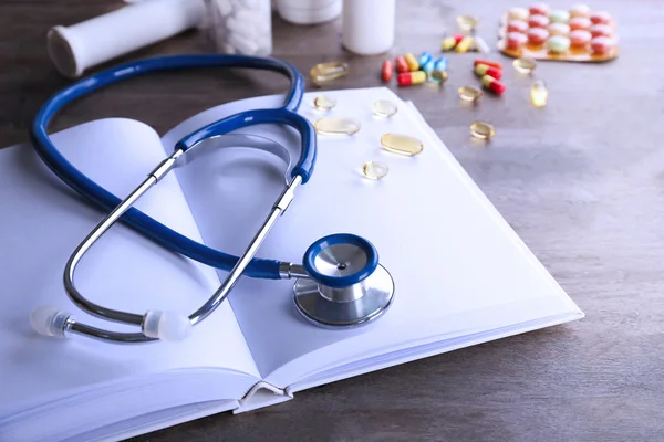 Stethoscope with open book and pills — Stock Photo, Image