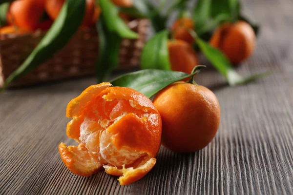 Peeled fresh tangerine with leaves and ripe mandarins on wooden table, closeup — Stock Photo, Image