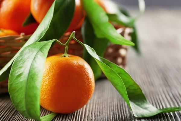 Tangerinas frescas com folhas na cesta na mesa de madeira, close-up — Fotografia de Stock