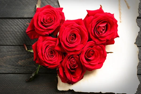 Brotes de rosas rojas frescas en forma de corazón con tarjeta regalo en blanco sobre fondo de madera — Foto de Stock