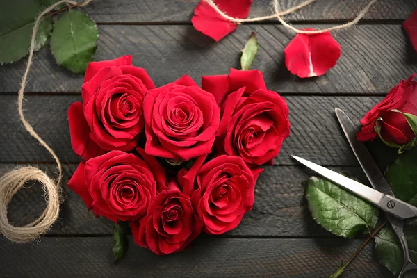 Brotes de rosas rojas frescas en forma de corazón con cuerda y tijeras sobre fondo de madera — Foto de Stock