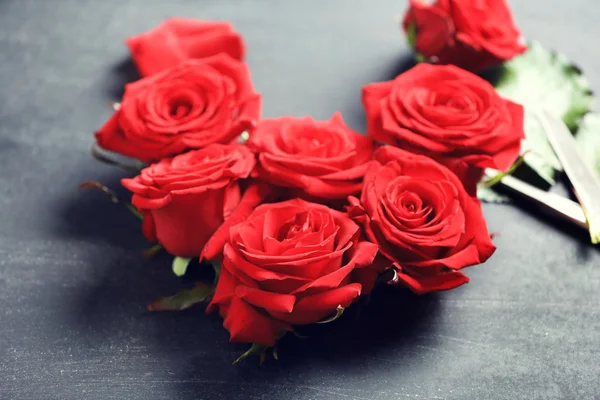 Brotes de rosas rojas frescas en forma de corazón con tijeras sobre fondo negro texturizado — Foto de Stock