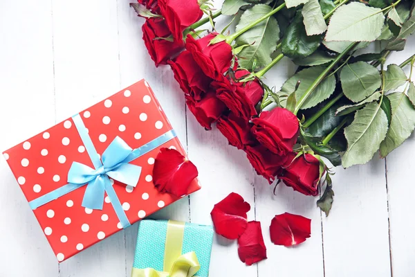 Belo buquê de rosas vermelhas e caixas de presente em fundo de madeira — Fotografia de Stock