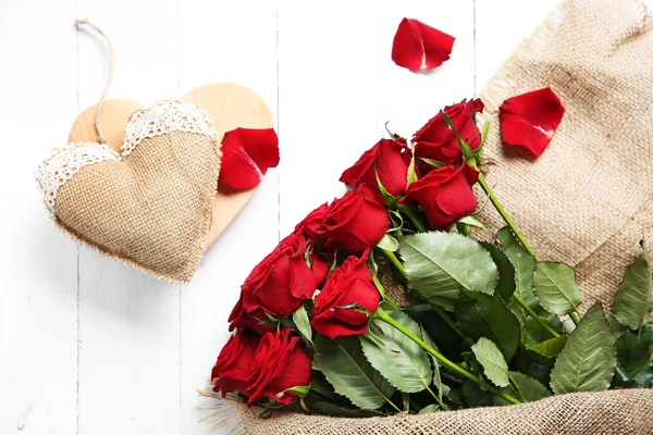Krásnou kytici rudých růží, zabalené do pytloviny srdcem na dřevěné pozadí — Stock fotografie