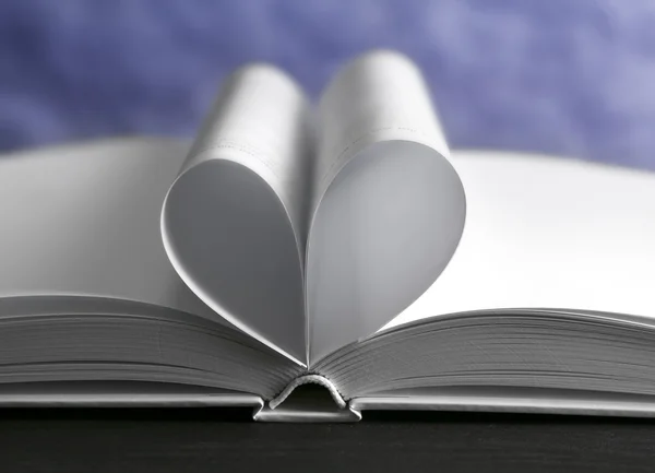 Sheets of book curved into heart shape on unfocused blue background — Stock Photo, Image