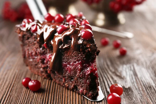 Stück Schokoladenkuchen mit Preiselbeeren auf Schaufel auf Holztisch, Nahaufnahme — Stockfoto