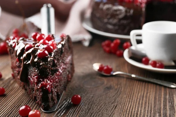 Pedazo de pastel de chocolate con arándanos en la pala y taza de té en la mesa de madera, primer plano — Foto de Stock