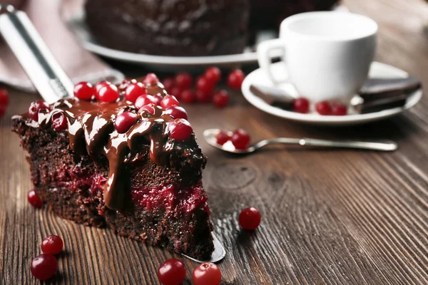 Stück Schokoladenkuchen mit Preiselbeeren auf Schaufel und Tasse Tee auf Holztisch, Nahaufnahme — Stockfoto