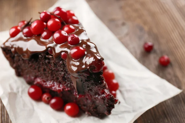 Piece of chocolate cake with cranberries on parchment, closeup — Stock Photo, Image