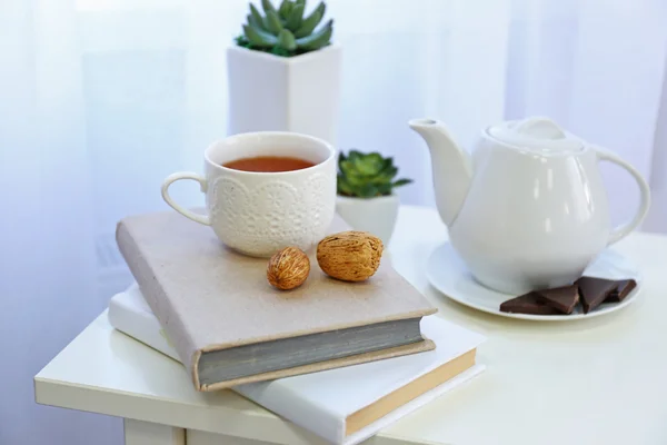 Livros, um bule de chá, uma xícara de chá e nozes na mesa na sala — Fotografia de Stock