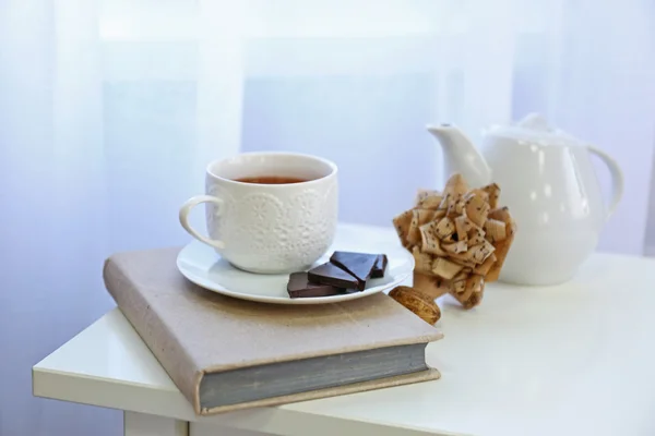 A cup of tea, chocolate, book and handmade paper flower on the table in the room — Stock Photo, Image