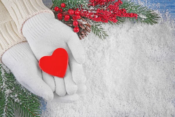 Frauenhände in Fäustlingen mit dekorativem Herz auf Schnee-Hintergrund — Stockfoto