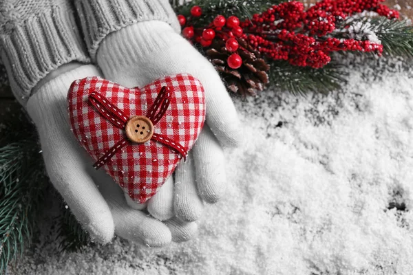 Mãos femininas em mitenes com coração decorativo no fundo da neve — Fotografia de Stock
