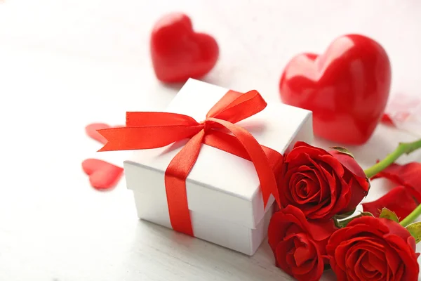 Scatola regalo, fiori di rosa e cuori decorativi su sfondo di legno chiaro — Foto Stock