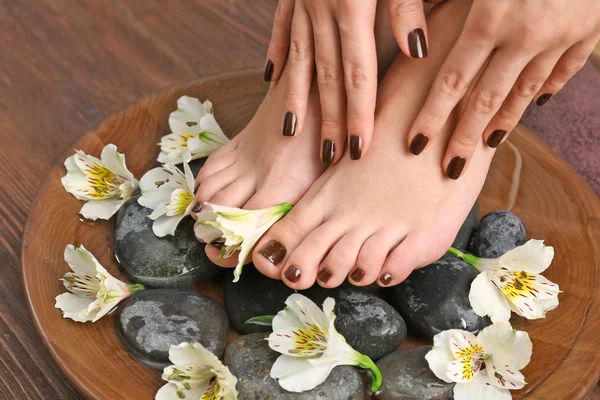 Gemanicuurde vrouwelijke voeten en handen in de houten kom spa met bloemen en water closeup — Stockfoto
