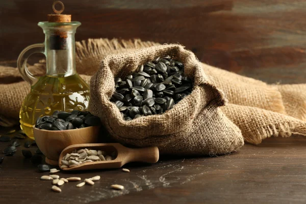 Sunflower seeds in bag and oil on wooden table background, closeup — Stock Photo, Image