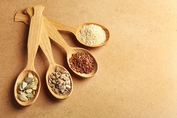 Sesame, flax, pumpkin and sunflower seeds in wooden spoons on beige background, closeup — Stock Photo, Image