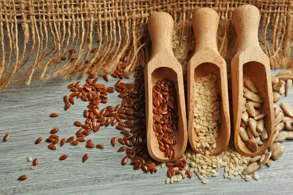 Sesame, flax and sunflower seeds in wooden spoons on table, closeup — Stock Photo, Image