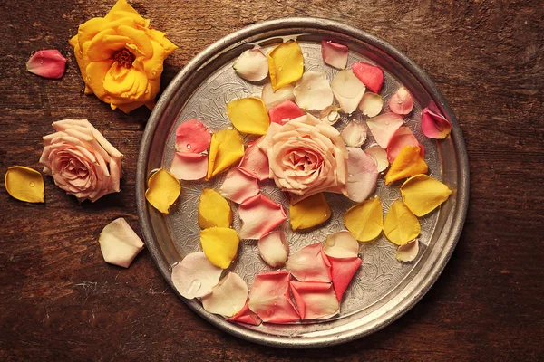 Pink and yellow rose petals in silver bowl with water on wooden background — Stock Photo, Image