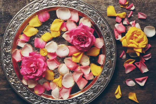 Rosa y amarillo pétalos de rosa en tazón de plata sobre fondo de madera — Foto de Stock