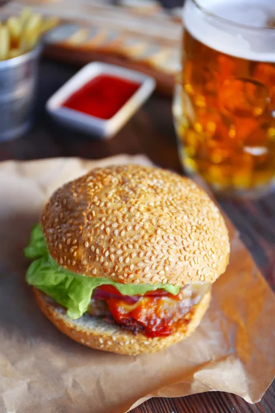 Gran hamburguesa sabrosa en un papel con cerveza ligera en taza de vidrio, de cerca — Foto de Stock
