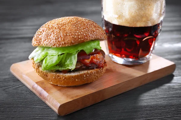 Taza de cristal de cerveza oscura con hamburguesa en la mesa de madera, de cerca — Foto de Stock
