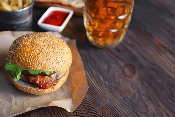Gran hamburguesa sabrosa en un papel con cerveza ligera en taza de vidrio, de cerca — Foto de Stock