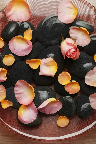 Rosa y amarillo pétalos de rosa en cuenco de cristal con agua y piedras negras, de cerca — Foto de Stock