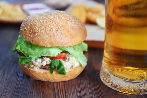 Gran hamburguesa sabrosa con taza de vidrio de cerveza ligera sobre fondo de madera oscura, de cerca — Foto de Stock