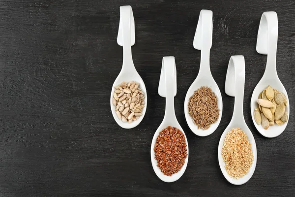 Diferentes tipos de sementes em colheres na mesa de madeira — Fotografia de Stock