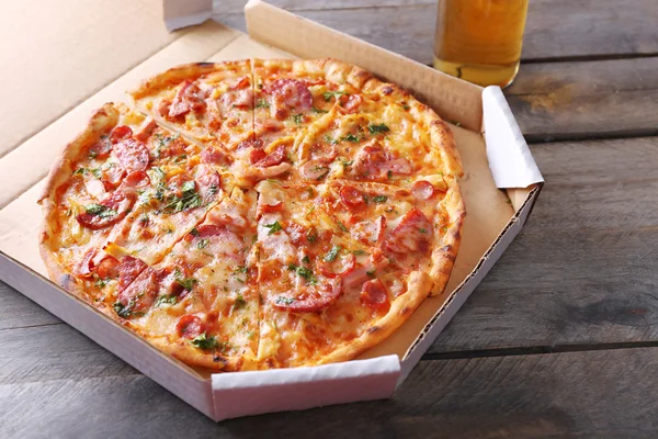 Sabrosa pizza en cartón y botella de cerveza están en la mesa de madera, de cerca — Foto de Stock