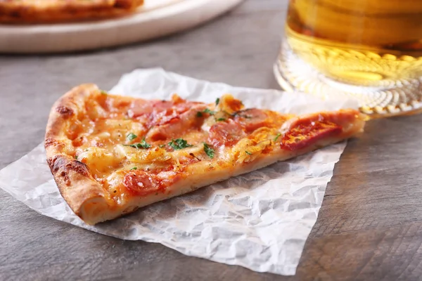 Piece of tasty pizza and glass of beer are on wooden table, close up — Stock Photo, Image