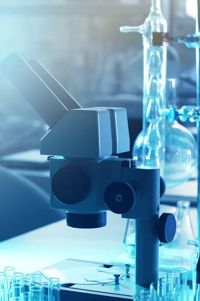 Microscópio e diferentes tubos de ensaio e frascos em laboratório — Fotografia de Stock