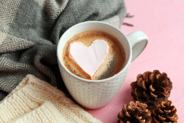 Cup of hot cappuccino with heart marshmallow and warm clothes on pink background, close up — Stock Photo, Image