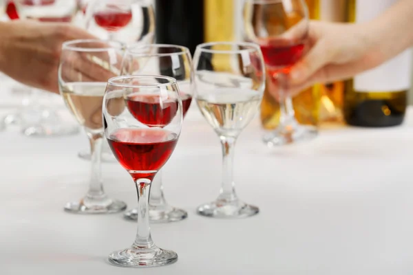Bicchieri con diversi tipi di vino e mani umane che tengono gli occhiali da vino sullo sfondo — Foto Stock