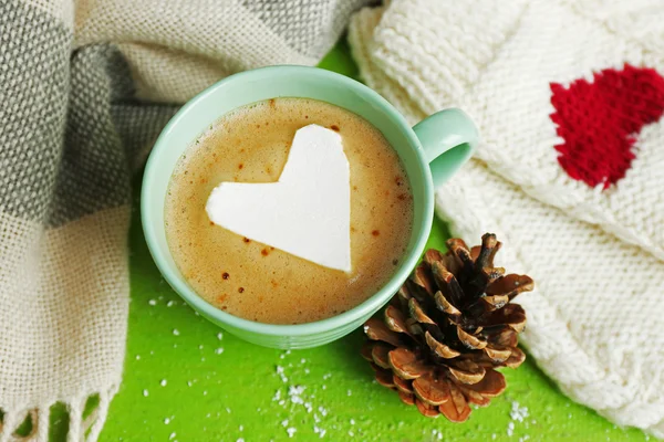 Xícara de cappuccino quente com marshmallow coração e roupas quentes no fundo verde, close-up — Fotografia de Stock