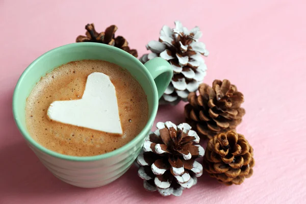 Xícara de cappuccino quente com coração marshmallow e pinhas em fundo rosa, close up — Fotografia de Stock