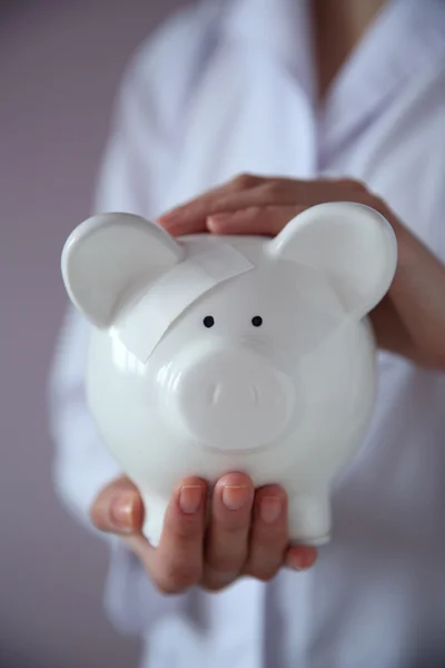 Woman holding in hands white piggy bank with patch — Stock Photo, Image