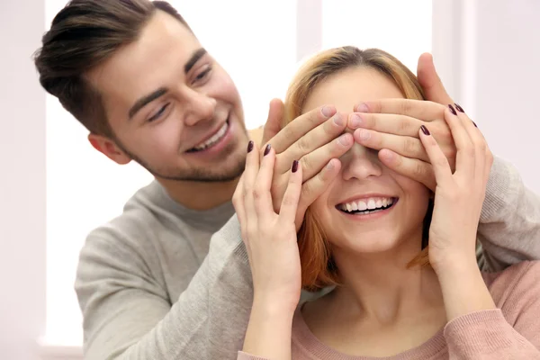 Junger Mann schließt die Augen seiner Freundin am Fenster — Stockfoto