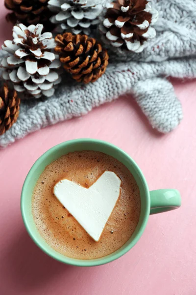 Tazza di cappuccino caldo con marshmallow cuore, guanti caldi e pigne su sfondo rosa, primo piano — Foto Stock