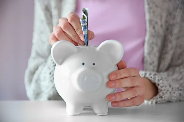 Mulher colocando nota de dólar no banco piggy branco na mesa — Fotografia de Stock