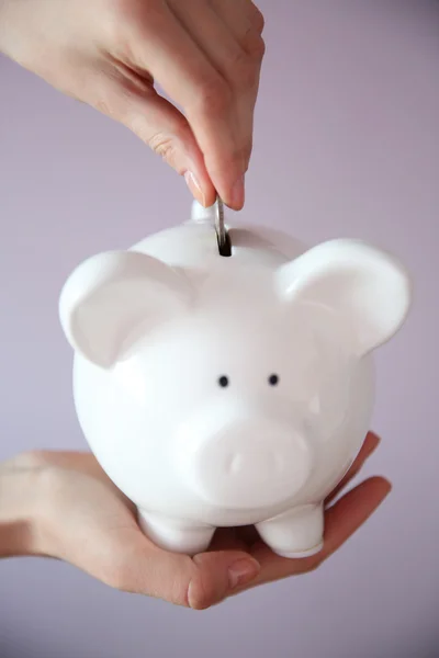 Mãos femininas segurando e colocando moeda no banco piggy branco, close-up — Fotografia de Stock