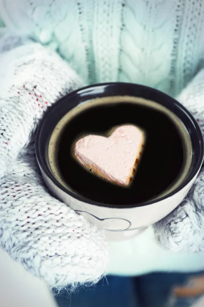 Mains féminines dans des mitaines chaudes tenant une tasse de café chaud avec guimauve cardiaque, gros plan — Photo