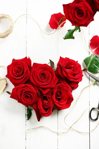 Fresh red roses buds in shape of heart with rope and scissors on wooden background Royalty Free Stock Images